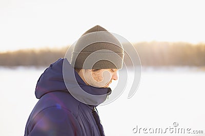 Adult european caucasian white male man in winter clothes on frozen lake. Side view, profile of young man against sun. Lifestyle Stock Photo