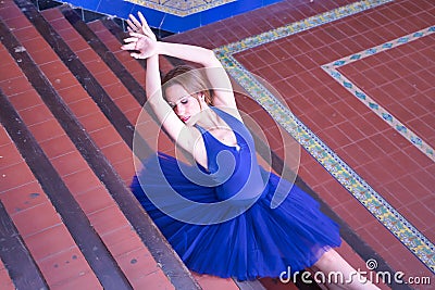 Adult female classical ballet dancer in blue tutu doing figures sitting on the steps of a staircase Stock Photo