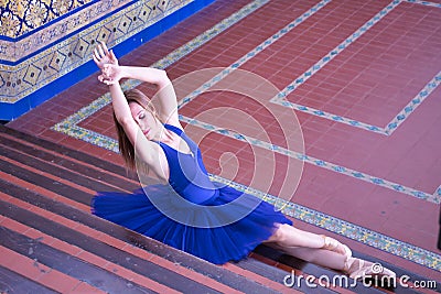Adult female classical ballet dancer in blue tutu doing figures sitting on the steps of a staircase Stock Photo