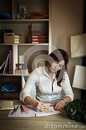 Adult female fashion designer draws a sketch in a cozy office Stock Photo