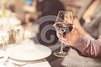 Adult hand holding glass of red whine. Toasting at celebration . Cafe or restaurant background. Chief speech while corporate busi Stock Photo