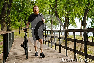 Adult handsome tattooed bearded smiling man i walking with bicycle Stock Photo