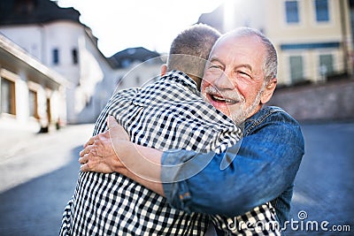 An adult hipster son and his senior father in town, hugging. Stock Photo