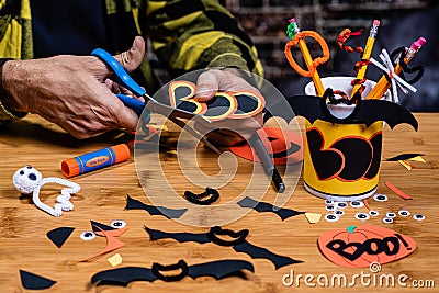 An Adult male cutting `Boo` from construction paper working on Halloween crafts at a table. Stock Photo