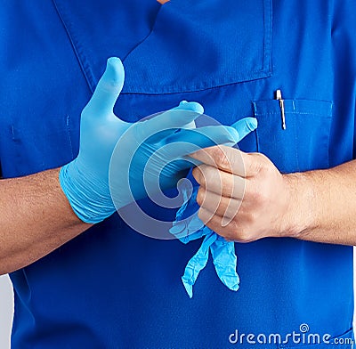 Adult male doctor in blue uniform puts on his hands blue sterile latex gloves Stock Photo