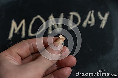 Adult male holding a piece of yellow chalk in his hand. Handwritten word MONDAY on black chalkboard. Days of the week. Calendar Stock Photo
