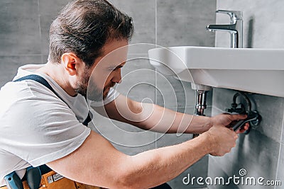 Adult male plumber in working overall fixing sink Stock Photo