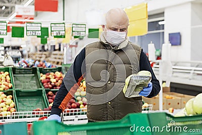 Adult man choosing vegetables at a supermarket with gloves and a mask on. Conscientious shopping during the virus outbreak Stock Photo