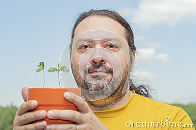 Adult man holds in his hands an orange pot with small sprouts Stock Photo