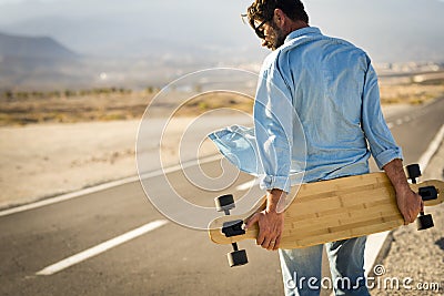 Adult man with long board table walking on a long asphalt street - concept of alternative modern people and travel transport free Stock Photo