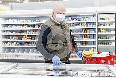 Adult man in the refridgerated goods area at a supermarket choosing products with gloves and a mask on. Conscientious shopping Stock Photo