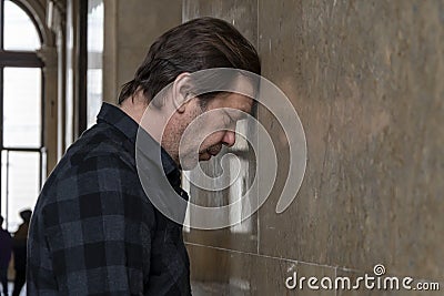 an adult man 40-50 years old with a beard, leaning against the wall. Concept: stressful situation, dismissal and troubles at work, Stock Photo