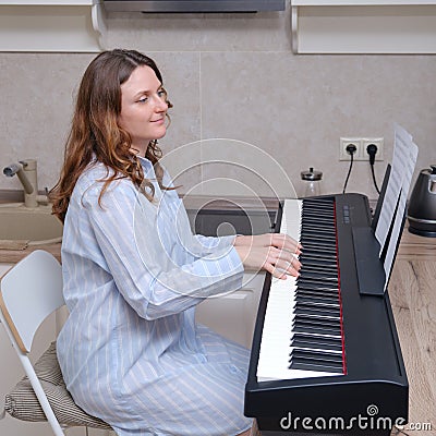 An adult woman in a blue nightgown plays music on a home piano Stock Photo