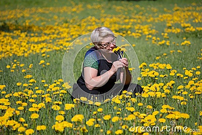 An adult woman, in a dandelion field, holds a yellow flower in her hand. Concept, pondered about the meaning of life, looks at nat Stock Photo