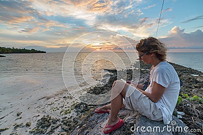 Adult woman with eyeglasses reading ebook relaxing at tropical beach dramatic sky holidays vacation concept Stock Photo