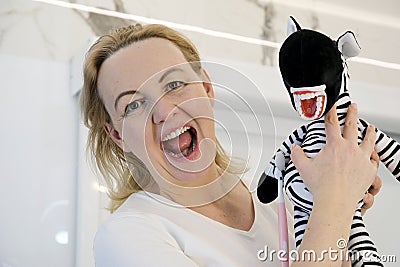 an adult woman in her hands with a toy zebra soft toy striped with real teeth false teeth woman laughs parodying a toy Stock Photo