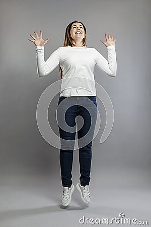Adult woman jumping. Smiling brunette in jeans and a white sweater. Happiness and positivity. Gray background. Vertical Stock Photo