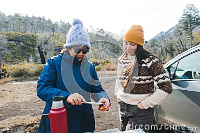 Adult woman, wearing warm clothes, preparing breakfast in makeshift table at countryside. Stock Photo