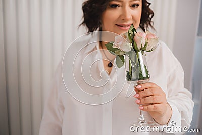 An adult woman in a white shirt is standing with a glass with roses sprinkled on it. A girl in the interior with a glass Stock Photo