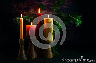 Advent arrangement with four candles in red and yellow on wooden holders and pine branches against a very dark background from Stock Photo