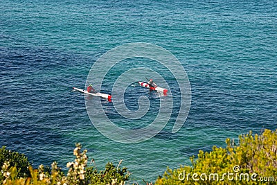 Adventure of paddling white and red kayaks in blue open water along coastline with vegetation. Editorial Stock Photo