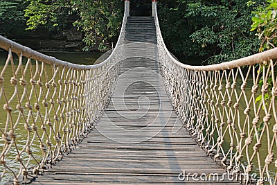 Adventure wooden rope suspension bridge crossing river Stock Photo