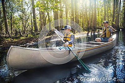 Adventuresome Father and son canoeing together on a beautiful river in a thick forest Stock Photo