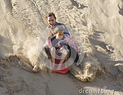 Adventuresome girls boarding down the Sand Dunes Stock Photo