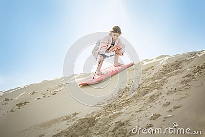 An adventuresome Little Girl boarding down the Sand Dunes Stock Photo