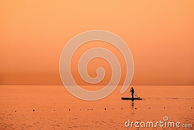 Adventurous people on a stand up paddle board is paddling during a bright and vibrant sunrise Stock Photo