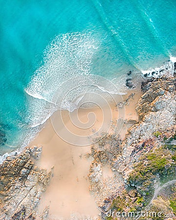 Aerial of a beach with beautiful waves, white sand and rocks at sunset Stock Photo