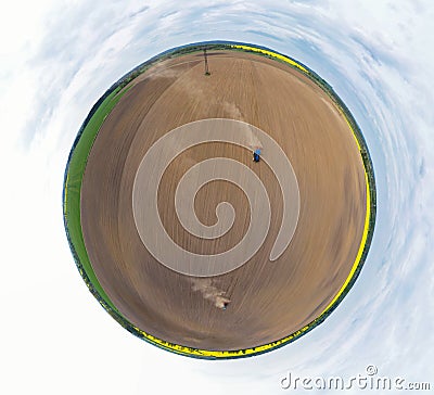 Aerial 360 degree panoramic view on blue tractor pulling a plow, preparing a soil for seed sowing, tractor making dirt cloud. Stock Photo