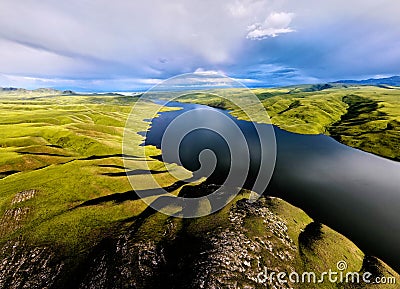 Aerial drone shot of beautiful scenery of blue mountain lake with green hills at sunset light glow in Tien Shan Mountains, Stock Photo