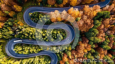 Aerial drone view of winding forest road in the middle of mountains. Colourful landscape with rural road, trees with yellow leaves Stock Photo