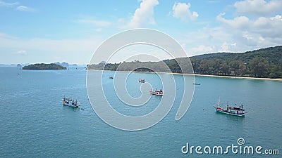 AERIAL: Fishing boats wait near sandy beach on a calm morning in stunning Krabi. Stock Photo