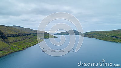 AERIAL: Flying above a large fish farm near remote coastal town in Faroe Islands Stock Photo