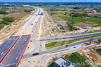 Aerial panorama top down view of an unfinished asphalt covered road with dirt, tracks of heavy machinery at construction site. The Stock Photo