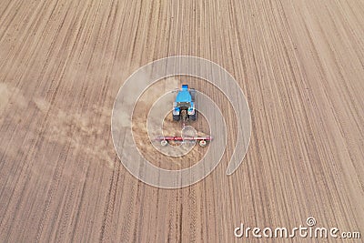 Aerial perspective view on blue tractor pulling a plow, preparing a soil for seed sowing, tractor making dirt cloud Stock Photo