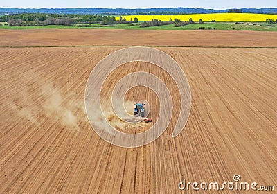 Aerial perspective view on blue tractor pulling a plow, preparing a soil for seed sowing, tractor making dirt cloud. Landmark on Stock Photo