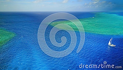 Aerial photo of a sailboat navigating through a tropical pass between reefs Stock Photo
