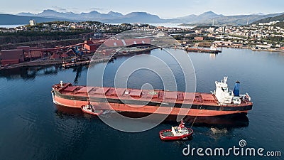 Aerial shot of a cargo ship approaching port terminal with help of towing ship Stock Photo