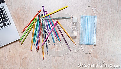 Aerial shot of colored pencils with disinfectant gel, mask and a laptop detail Stock Photo