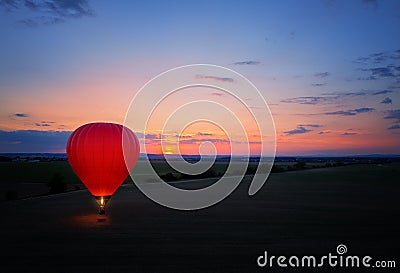 Aerial, side view of the evening landing of shining red-blue hot air balloon against sunset. Red hot air balloon firing its burner Stock Photo