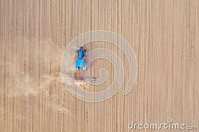 Aerial top down view on blue tractor pulling a plow, preparing a soil for seed sowing, tractor making dirt cloud Stock Photo