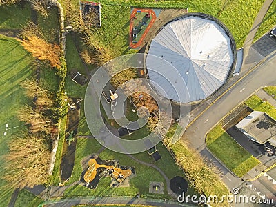 Aerial top view on a triangle shape public children playground with slide, climbing wall and swings, by a round play schooll with Stock Photo