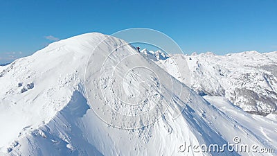 AERIAL: Unrecognizable skier hiking up the snowy mountain in sunny winter. Stock Photo