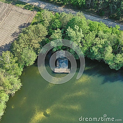 Aerial view of the corner of a pond with a small wooden fishing hut and a landing stage, trees at the bank Stock Photo