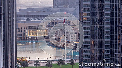 Aerial view of Dubai Fountain in downtown with palms in park next to shopping mall and souq night to day timelapse, UAE Stock Photo