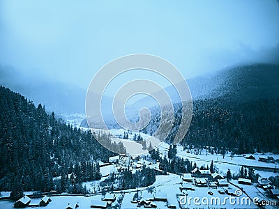 Aerial view of foggy countryside and houses in snowy valley. Hills and mountains with pine tree forest covered in snow Stock Photo