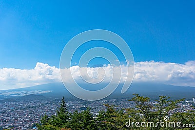 Aerial view of Fujiyoshida town and Mount Fuji peaking over clouds on sunny day Stock Photo